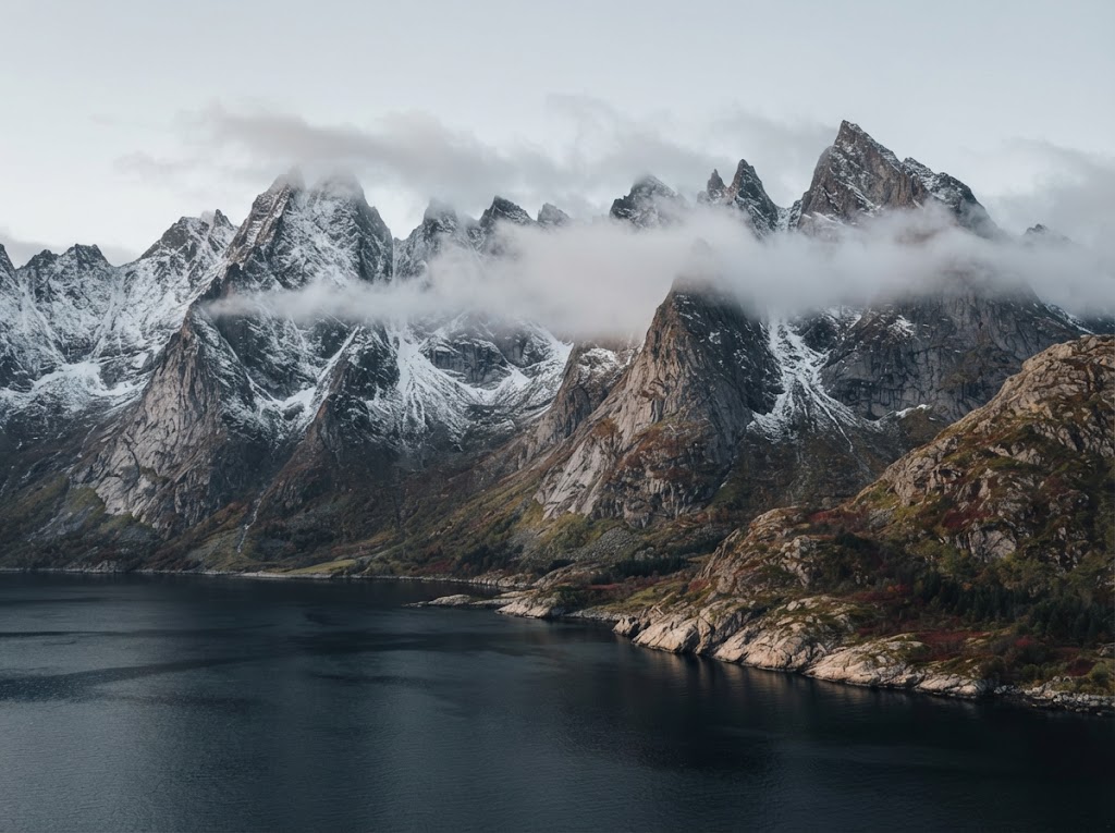 Artist's impression of sharp snow-dusted peaks of the Sunnmøre Alps rising above a dark fjord, cloud along the ridges